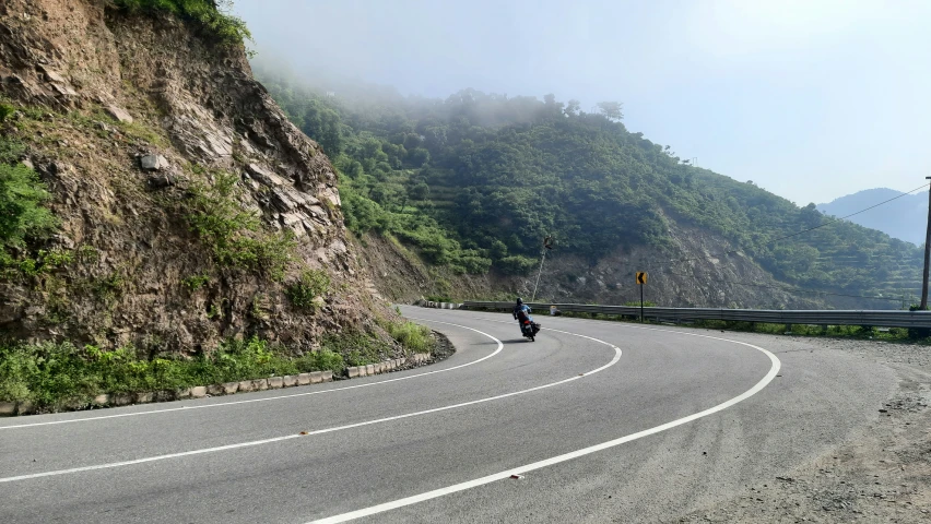 motorcycle rider on road with steep mountains in the background