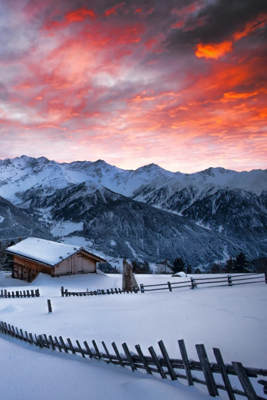 a house in the mountains at sunset with snow on the ground