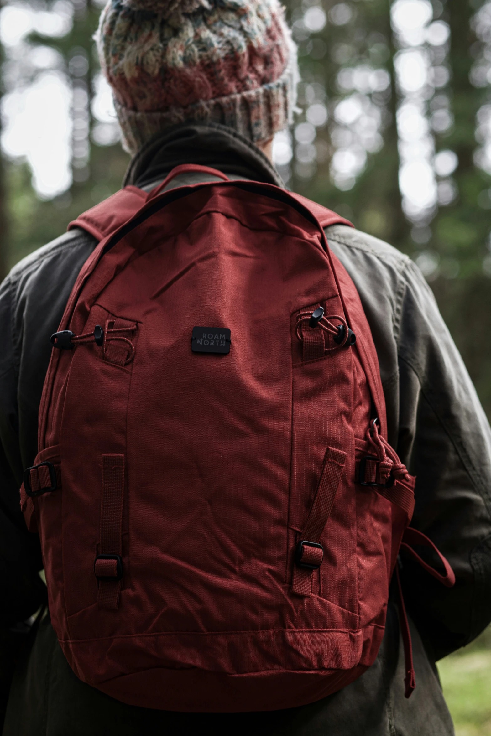 a man with his back turned to the camera, wearing a red backpack in the woods