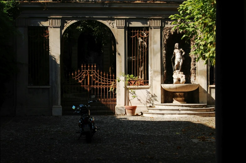 a motorcycle parked in a shady courtyard with an outside fountain