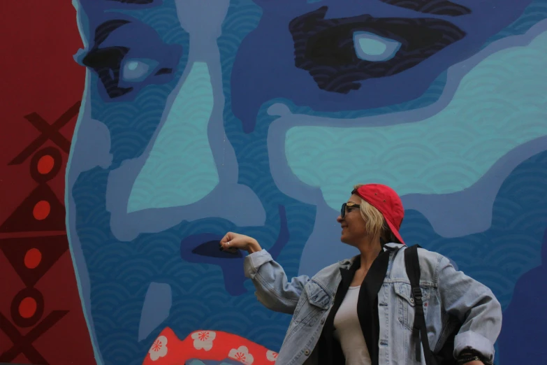 a woman stands near a colorful mural with blue eyes