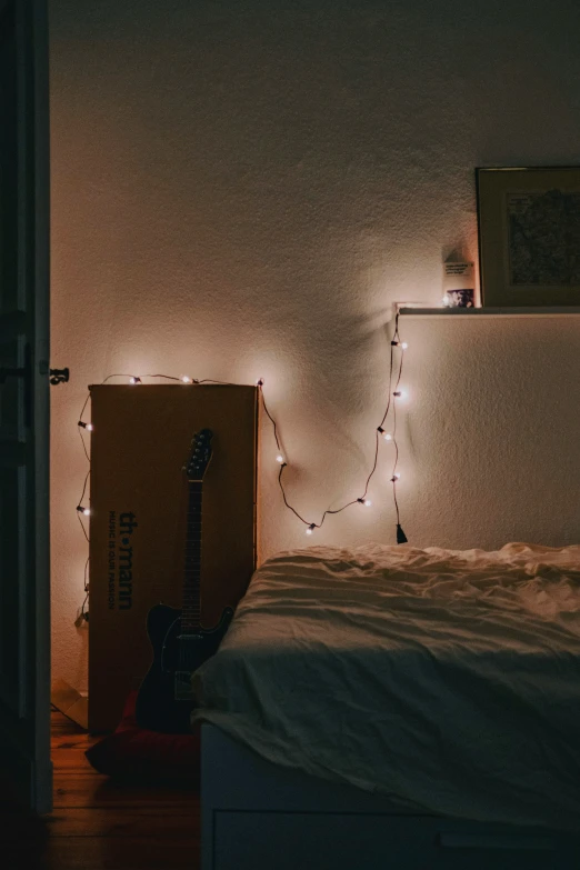 a dark room with the light on, a guitar is laying under the bed
