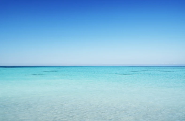 a beach scene with clear water and some boats out to sea