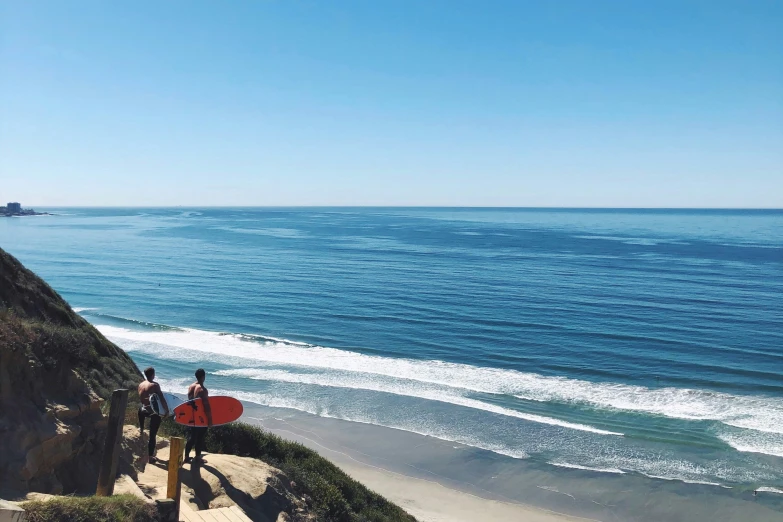 two surfers walk down the cliff towards the beach