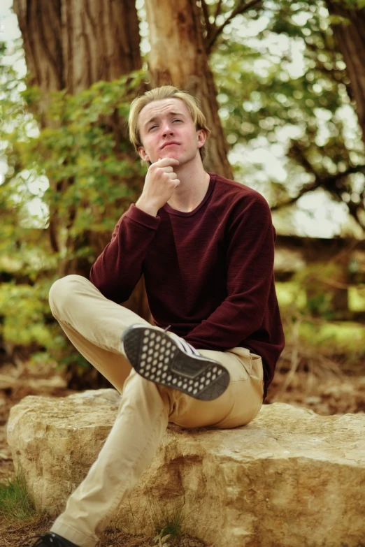 a man sitting on a rock with his hand on his chin