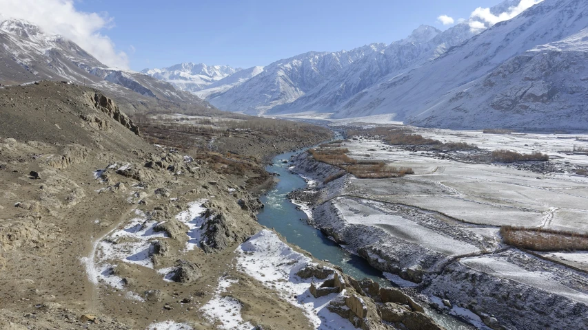 a mountain range next to a river with snow covering it