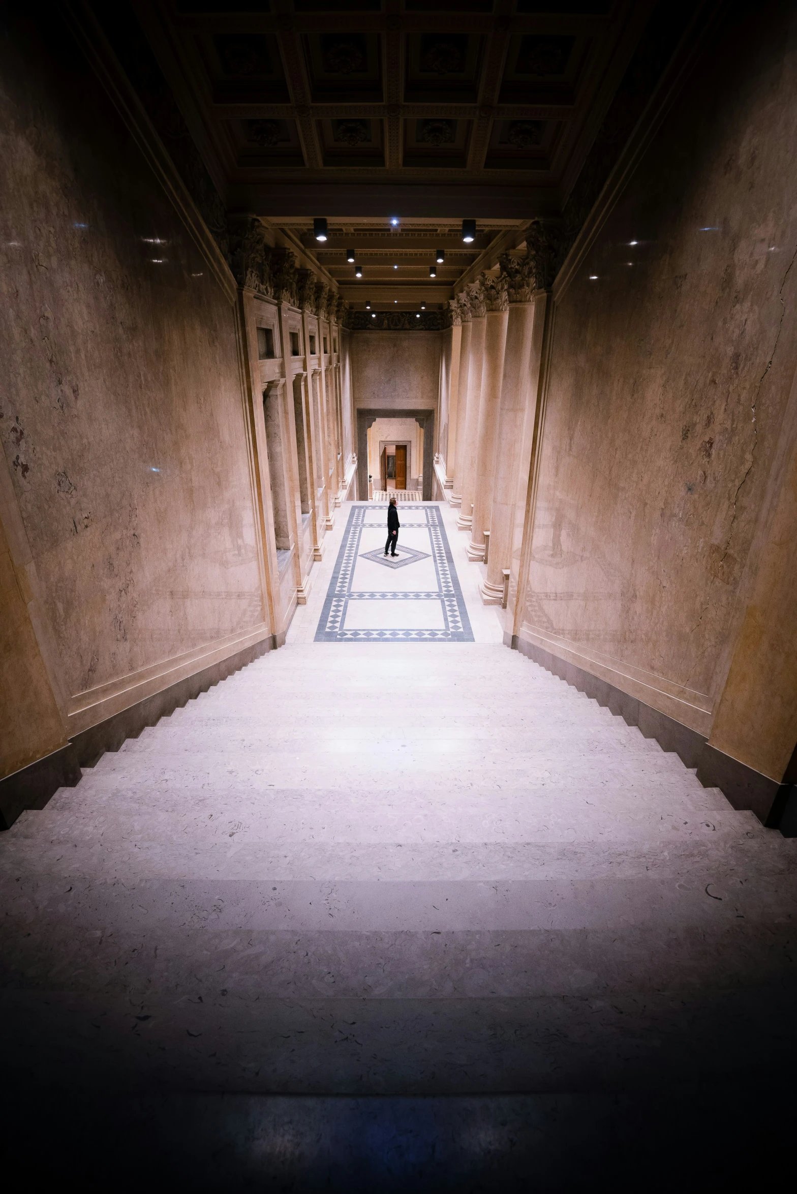 a woman walking down a stone hall with a mosaic tiled floor