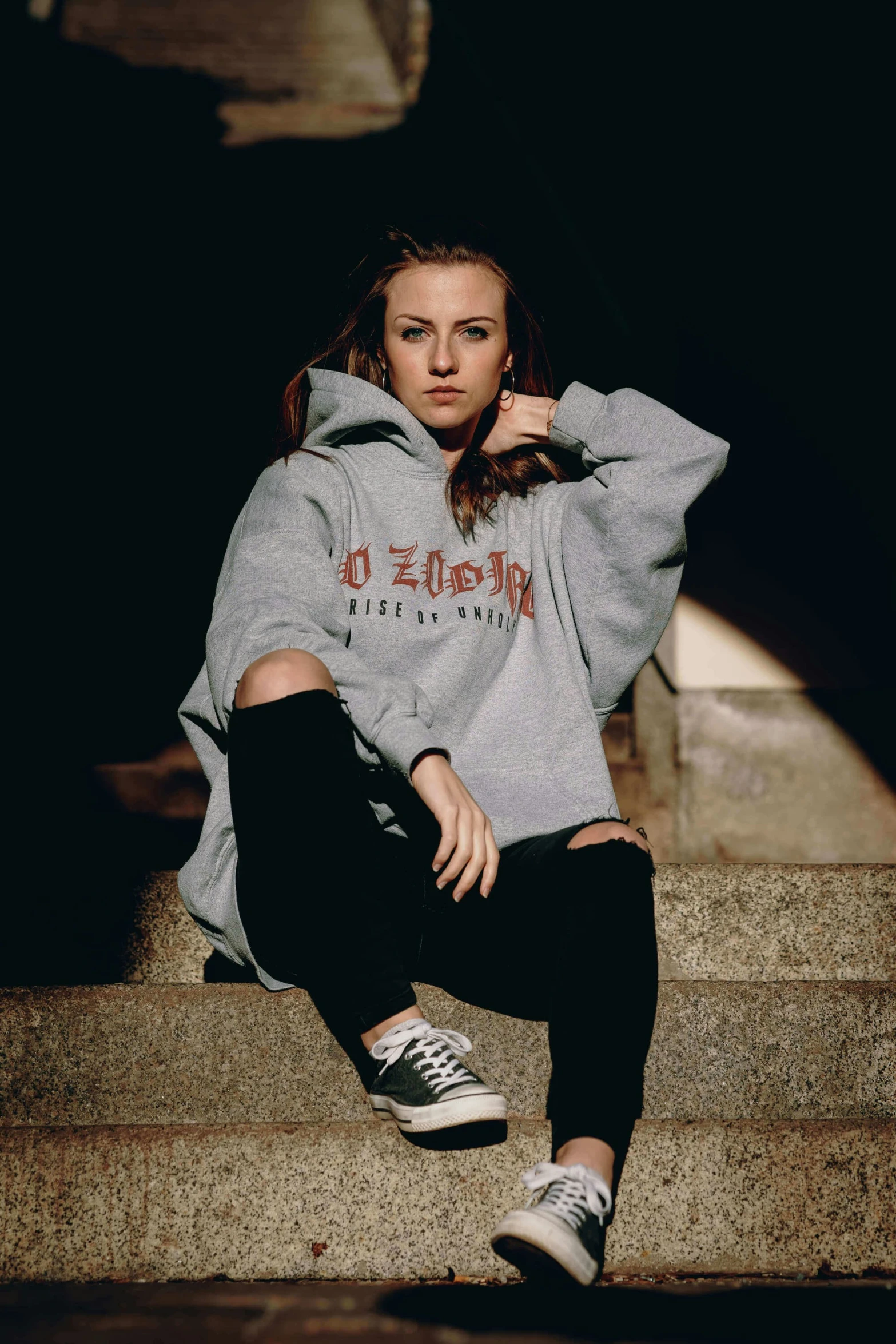 a girl in a grey hooded sweatshirt sits on stairs