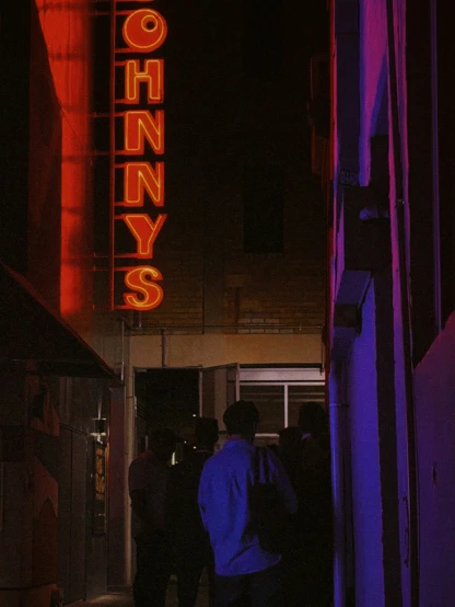 people are standing near a building with a neon sign above it