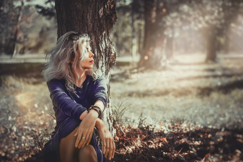 an old woman sitting underneath a tree in the forest