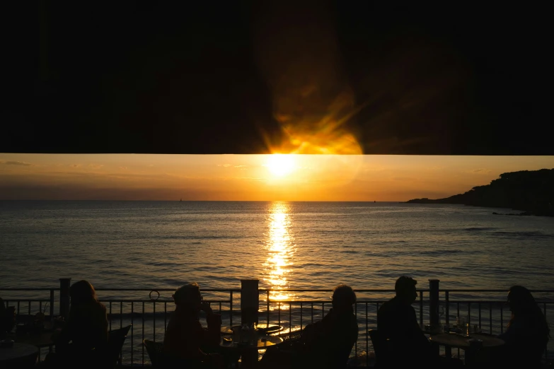 people are sitting at the end of an outdoor patio near the ocean