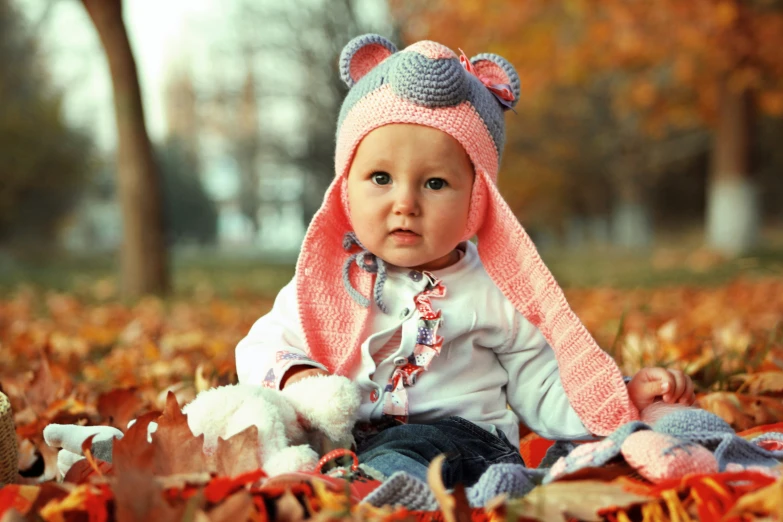 a baby with a knitted animal hat is sitting in the leaves