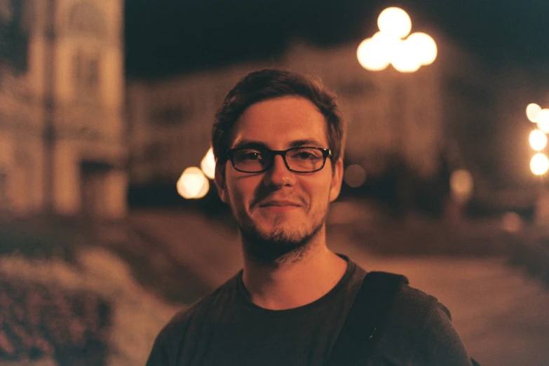 a man with glasses standing outside at night