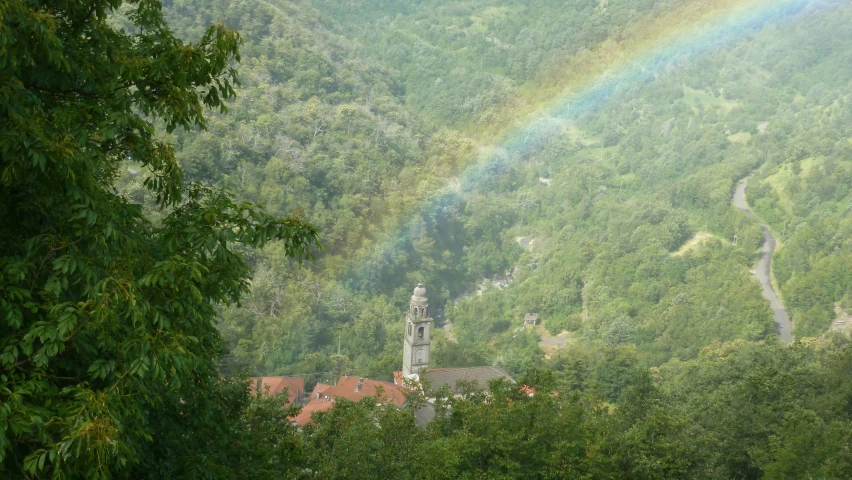 a tree line with a house and a rainbow in the distance