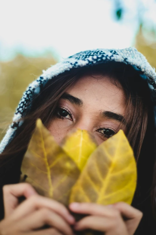 a woman in hoody covering her face with leafs
