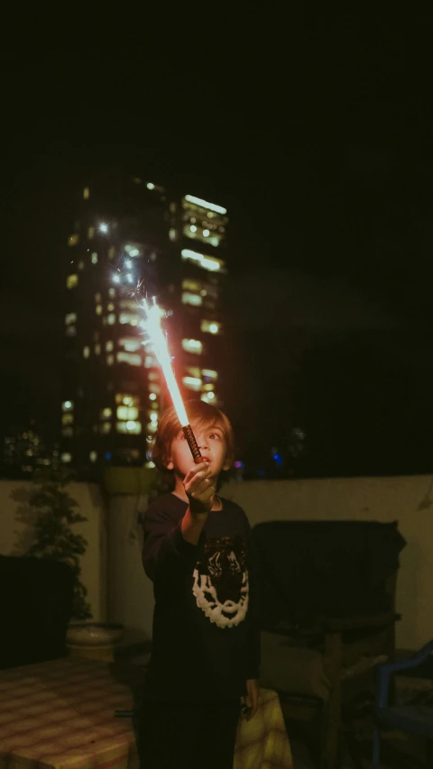 a little boy is holding a lighter with a city skyline behind him