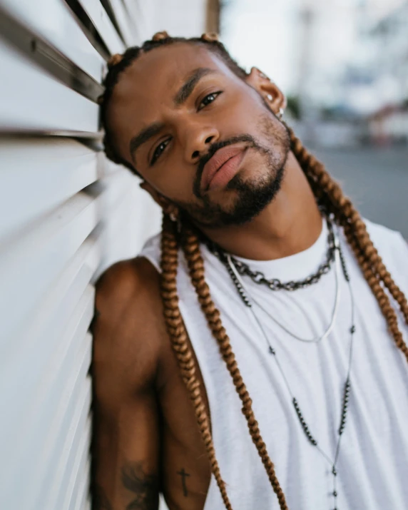 a young man with long blonde dread locks stands in front of a white wall