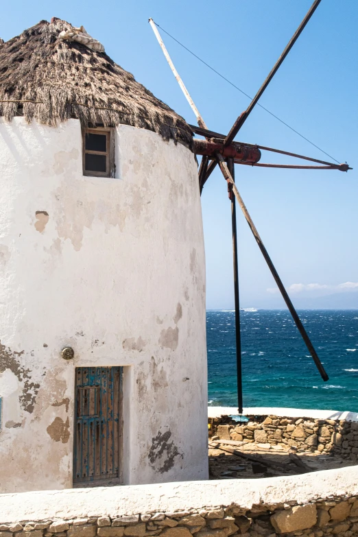 a windmill with a thatch roof in front of an ocean view