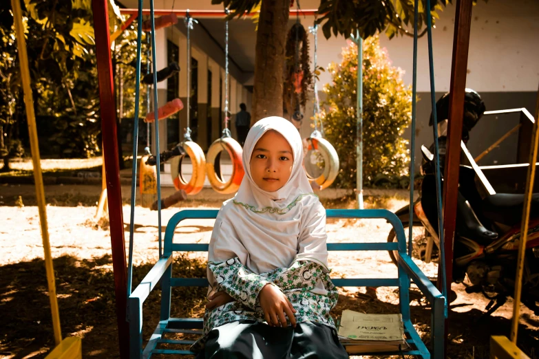 a girl sitting on a swing in front of a playground