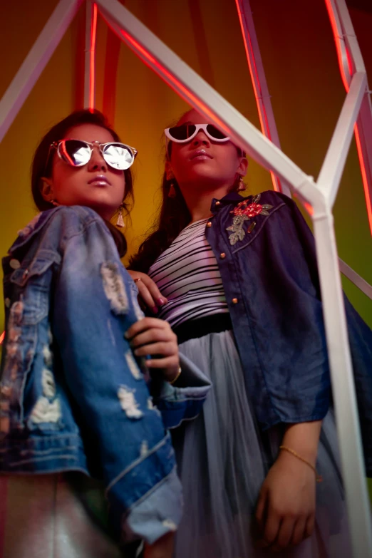 two young women, one wearing sunglasses, both standing behind glass