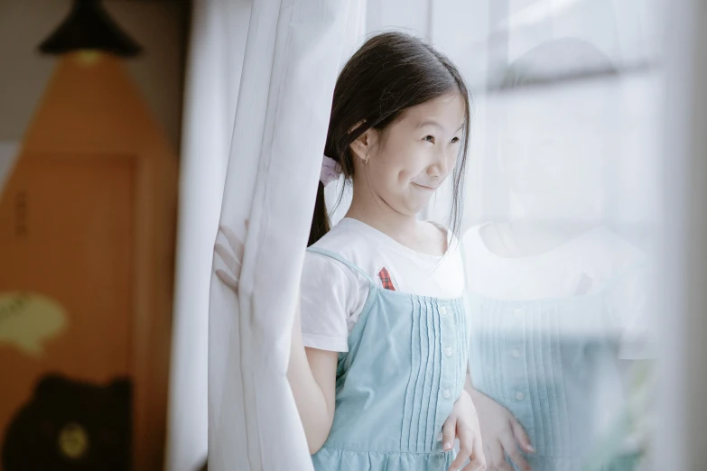 a little girl with brown hair is standing in front of a window
