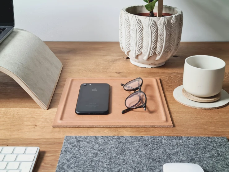 a cup and pair of sunglasses are on a wooden desk next to an iphone