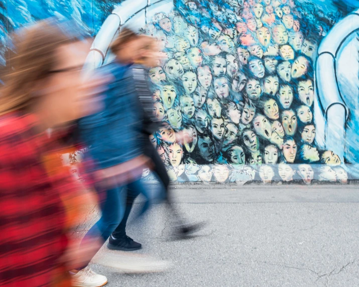 several people walking in front of an image on the side of a building