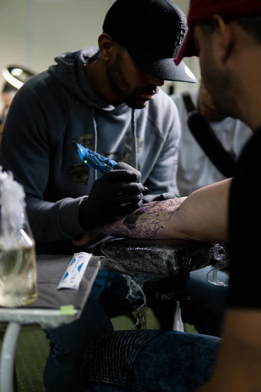 two men sitting in a room working on their tattoos