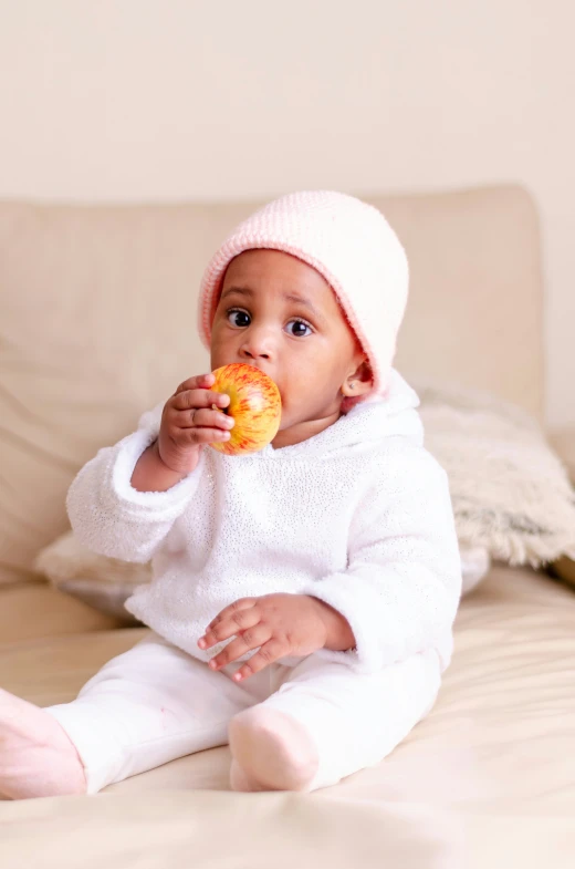 a baby is sitting on a bed holding an apple and a donut