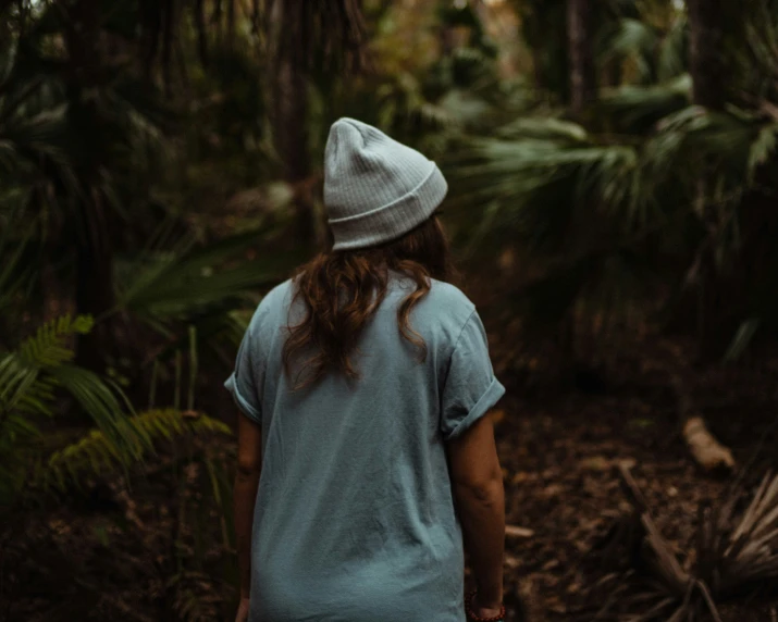a girl walks through a forest wearing a hat