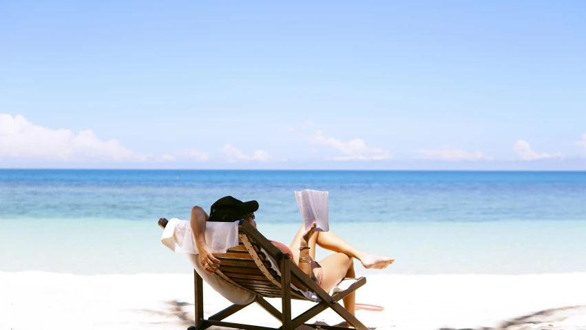 a woman reading on a deck chair with the ocean in the background