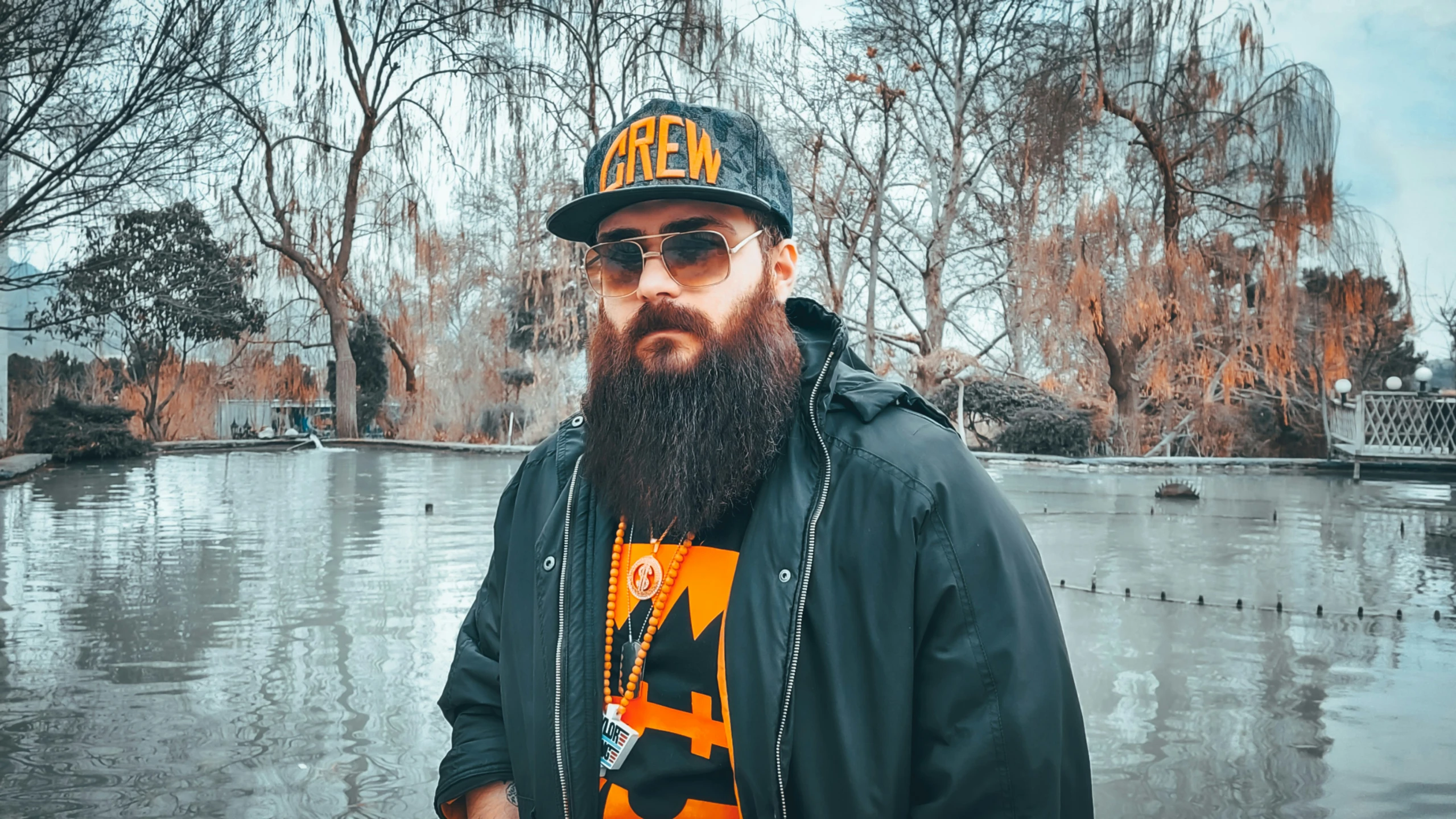 man in hoodie standing with water and trees in the background