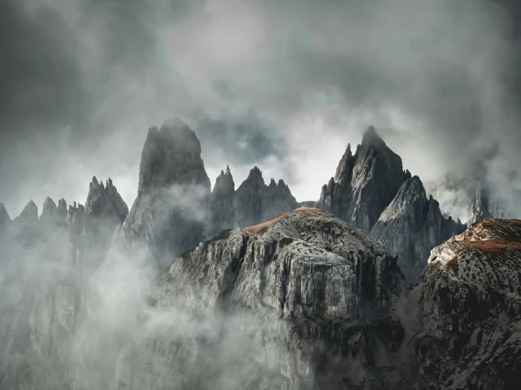 a mountain landscape that has some rocky mountain tops in the clouds