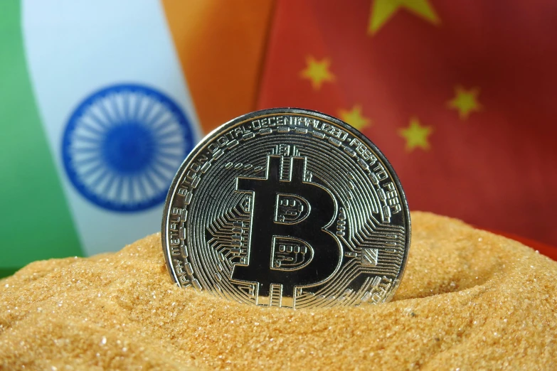 a bit coin sitting in the sand with china and indian flags