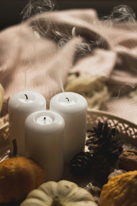 three white candles sitting next to pine cones