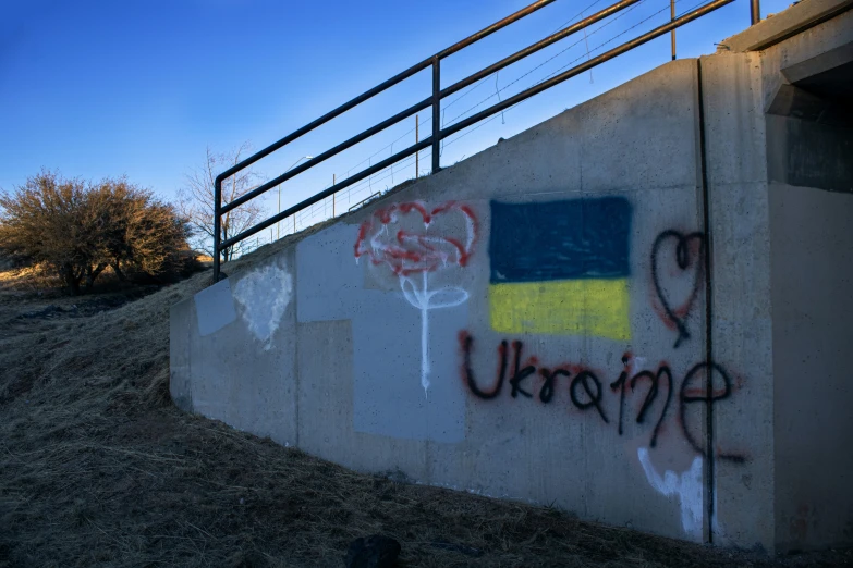 graffiti on the side of a cement wall with a railing on the top and trees in the distance