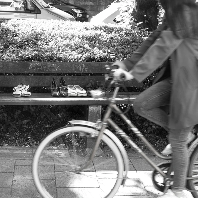 a black and white po of a woman sitting on a bench, while looking at a few other shoes on the ground and a bicycle in front