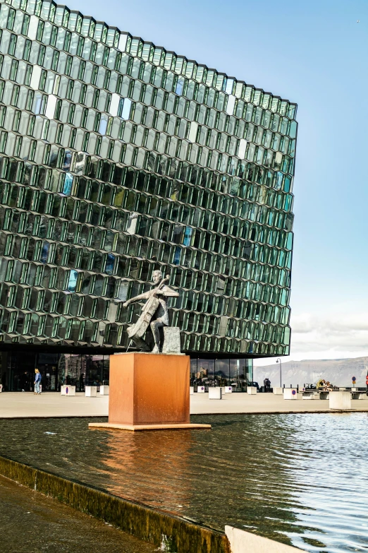 an artistic building next to water, with a statue in front