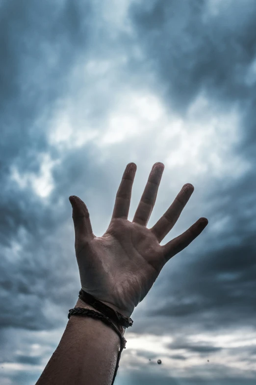 hand reaching for a dark cloud covered sky