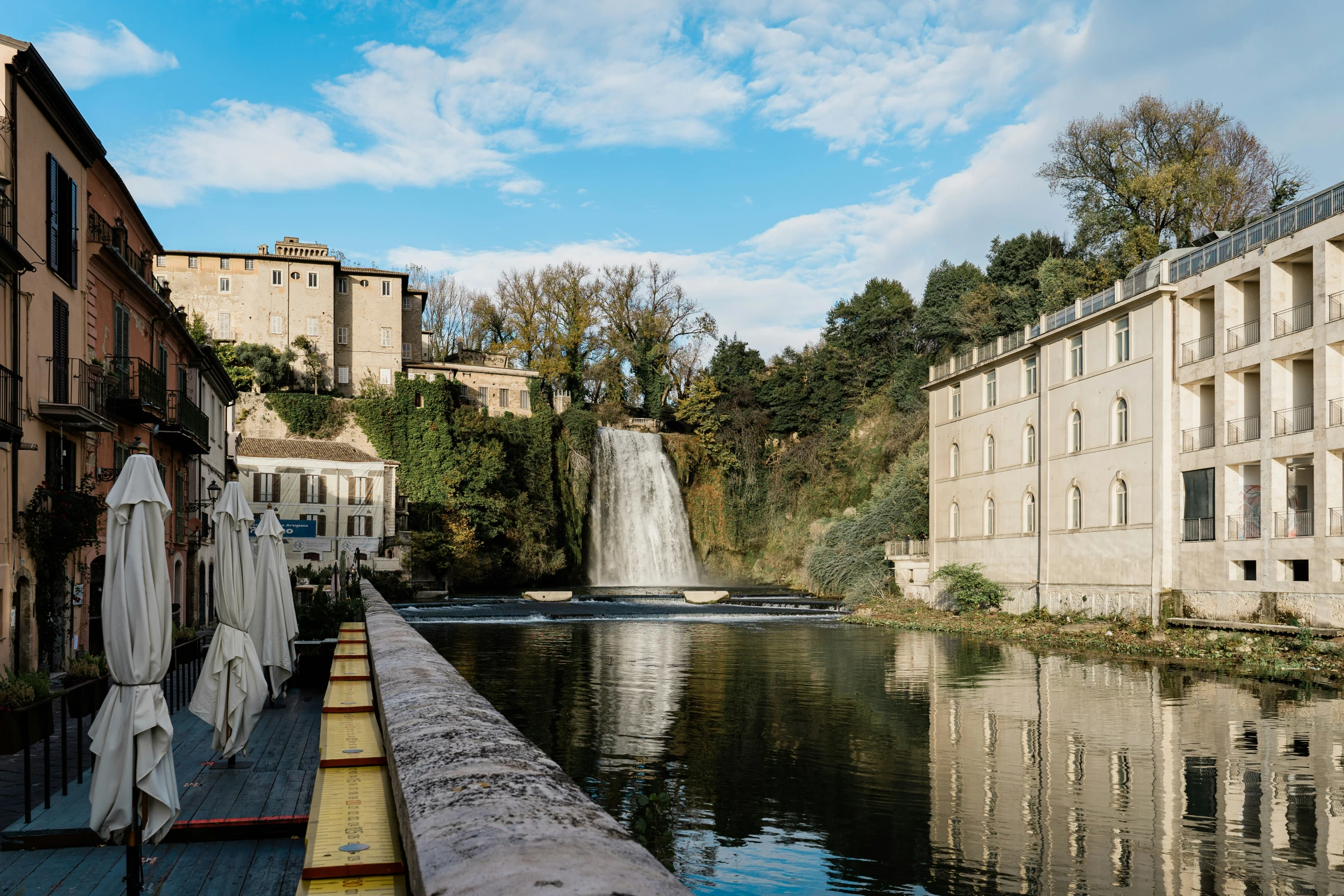 the waterway has many buildings and a waterfall in the background