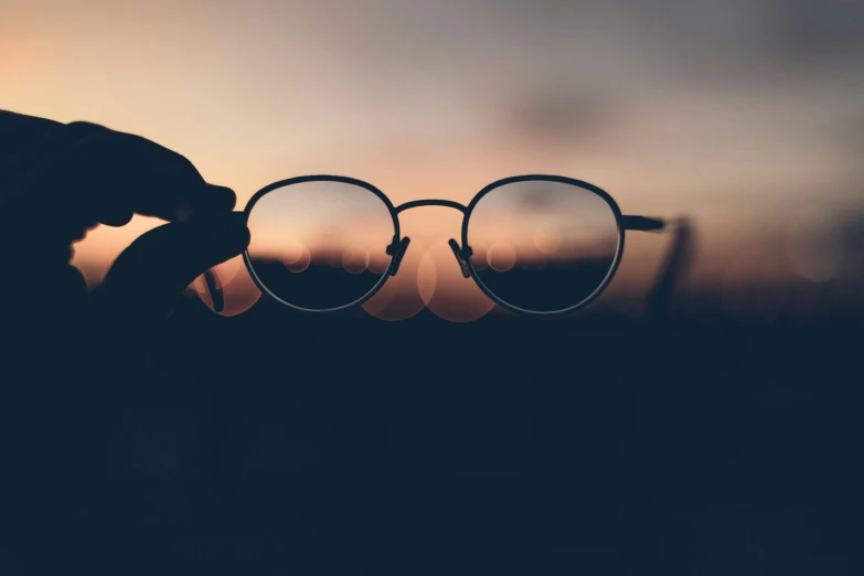 a person holding two glasses over a pair of dark colored glasses