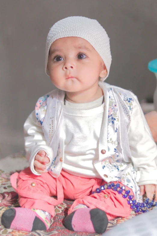 a baby wearing a white hat and sitting on the floor