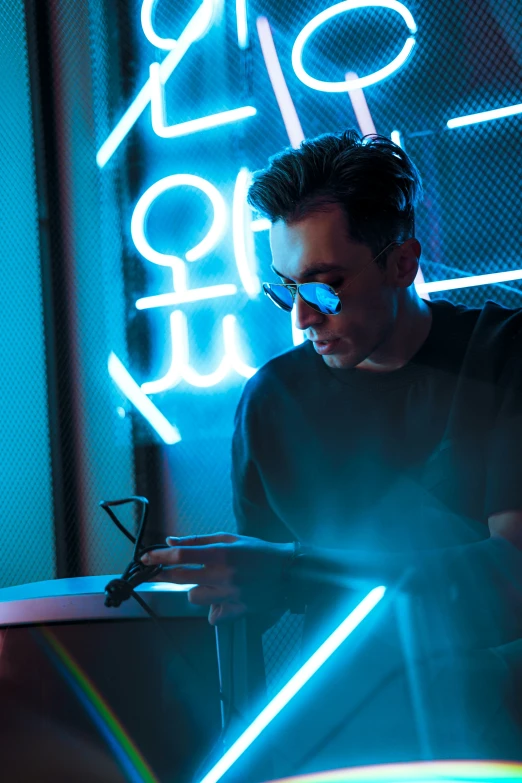 a man looks at his cell phone in front of a neon sign