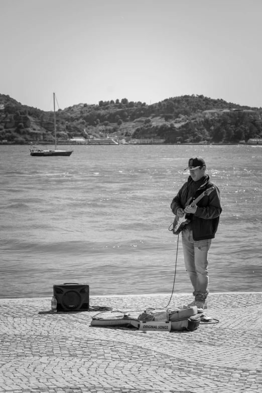 man with electric guitar on rocky area beside water