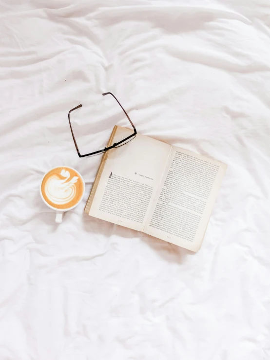 an open book with glasses on top and coffee on the side