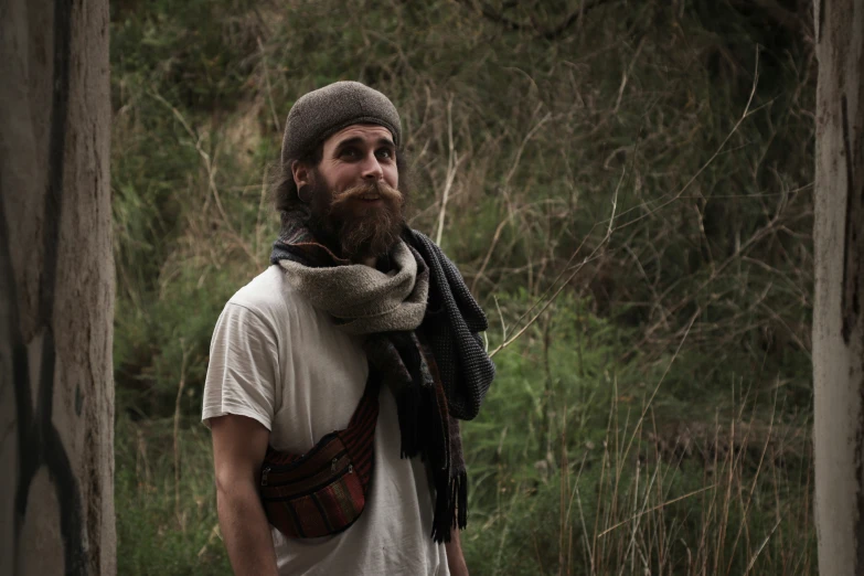 a man wearing a beanie and scarf standing in a wooded area