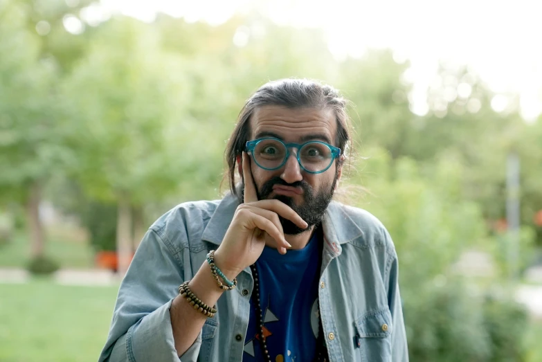 a man with long hair and blue glasses is holding a black necklace