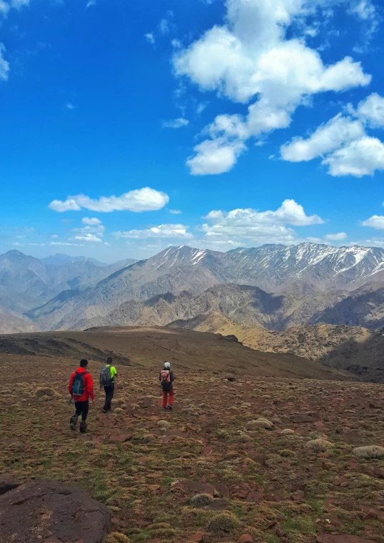 a group of hikers walk down a hill toward the mountains