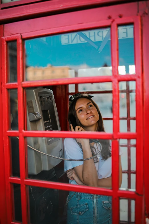 a smiling woman is seen through a phone booth