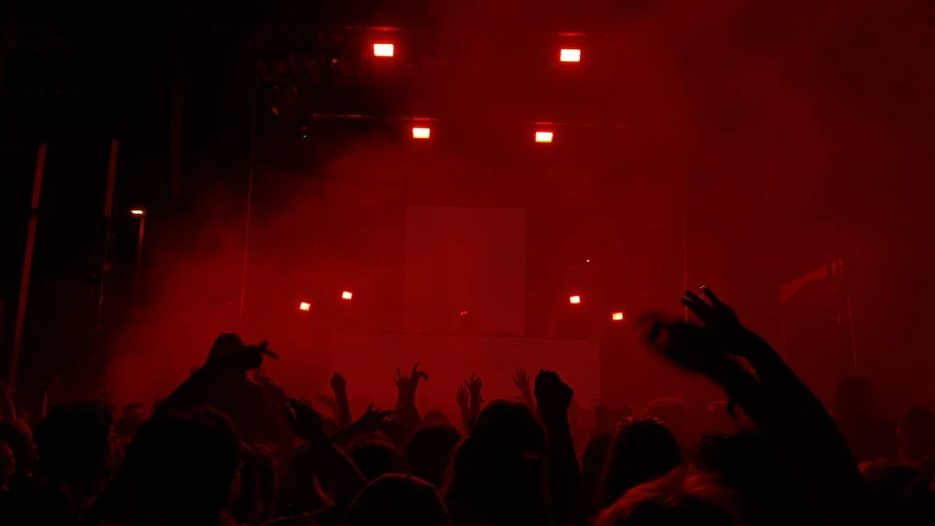 people at a concert with their arms up and arms raised in front of bright red smoke and smoke coming out of the stage